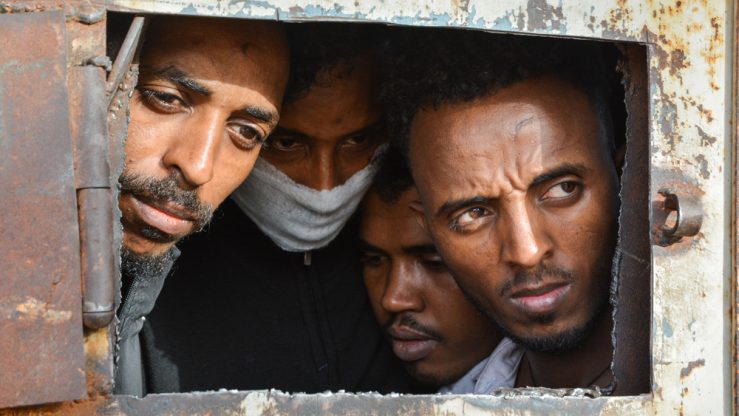 Migrants and refugees in Zintan and Gharyan detention centres in Refugees in Zintan DC at the gate of the main warehouse where 700 of them were detained.
A tuberculosis outbreak has likely been raging for several months in the detention centre and some wear masks for fear of contamination.
The main warehouse was emptied in June 2019, and the remaining people distributed among the other buildings within the detention centre compound.